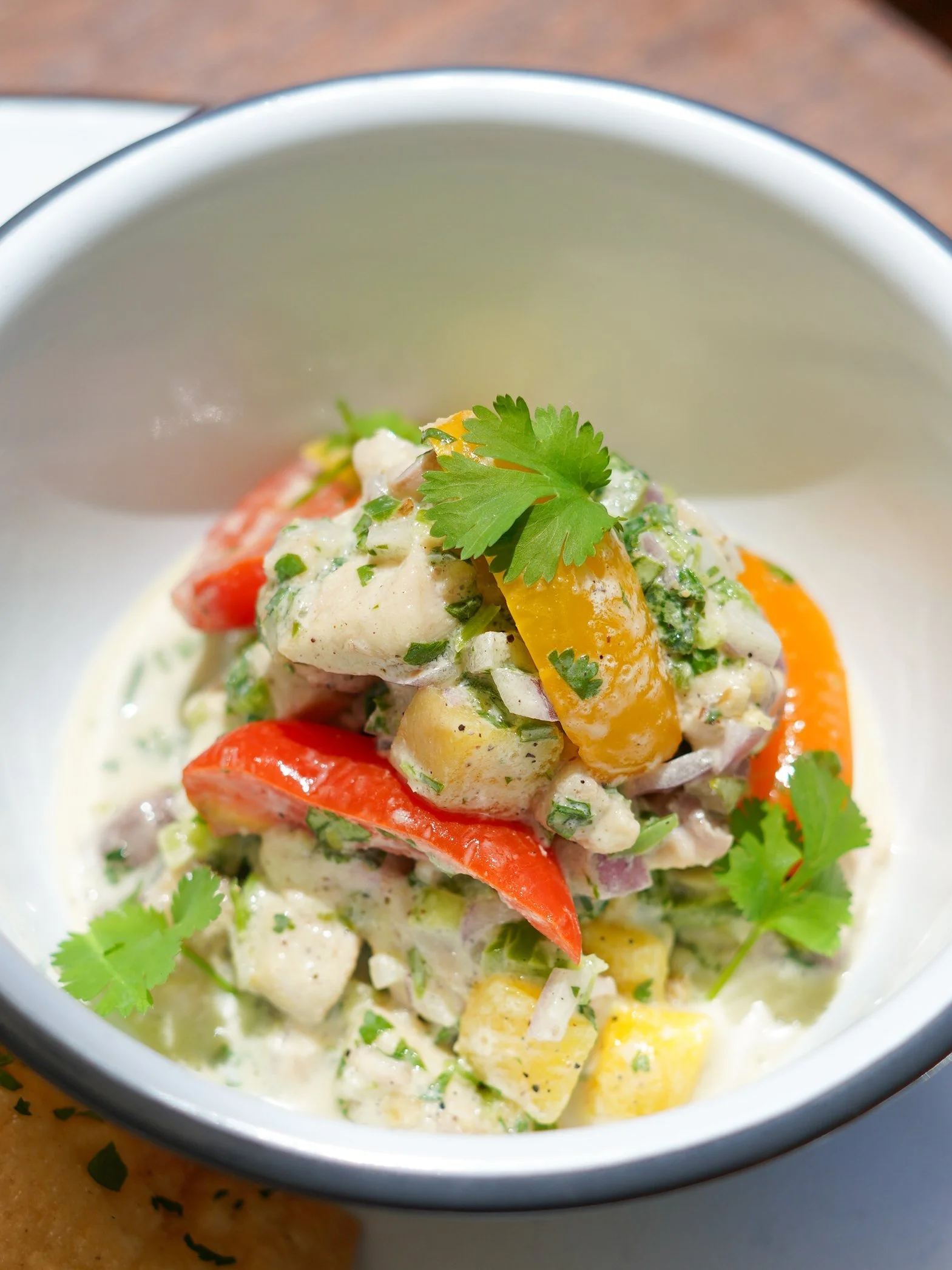 A bowl of potato salad topped with cilantro and garnished with slices of red bell pepper and yellow bell pepper.