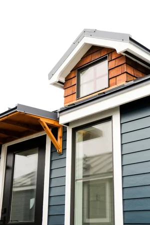 Close-up of a modern house with dark blue siding, large windows, and a small gable roof with wooden supports and a shingled dormer.