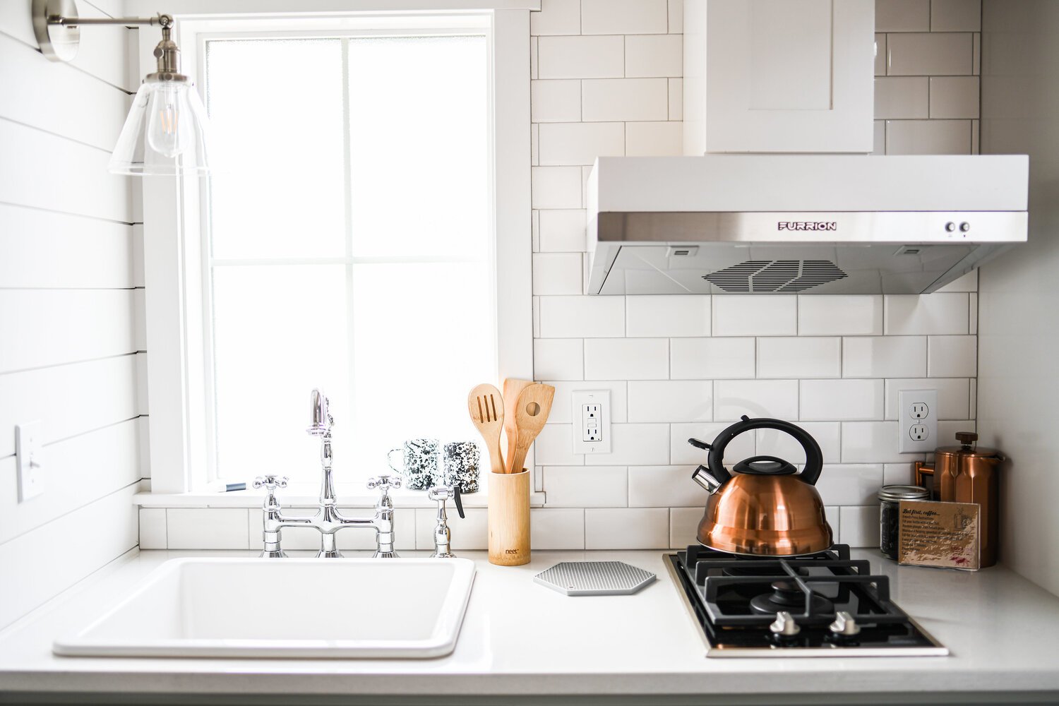 Modern tiny house kitchen with white subway tile backsplash, farmhouse sink, and a copper tea kettle.