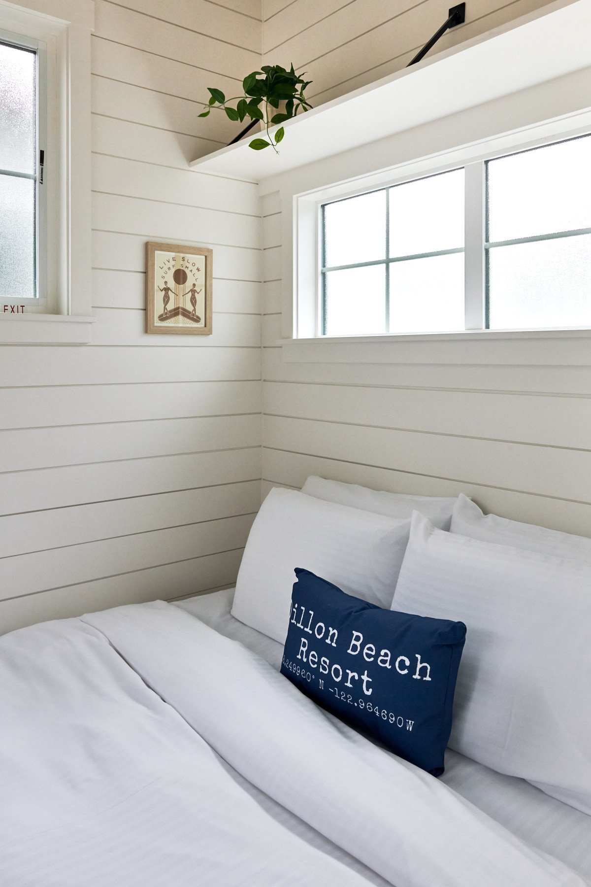Tiny house bedroom with white shiplap walls, a comfortable bed, and a "ブライトリビエラ" decorative pillow.
