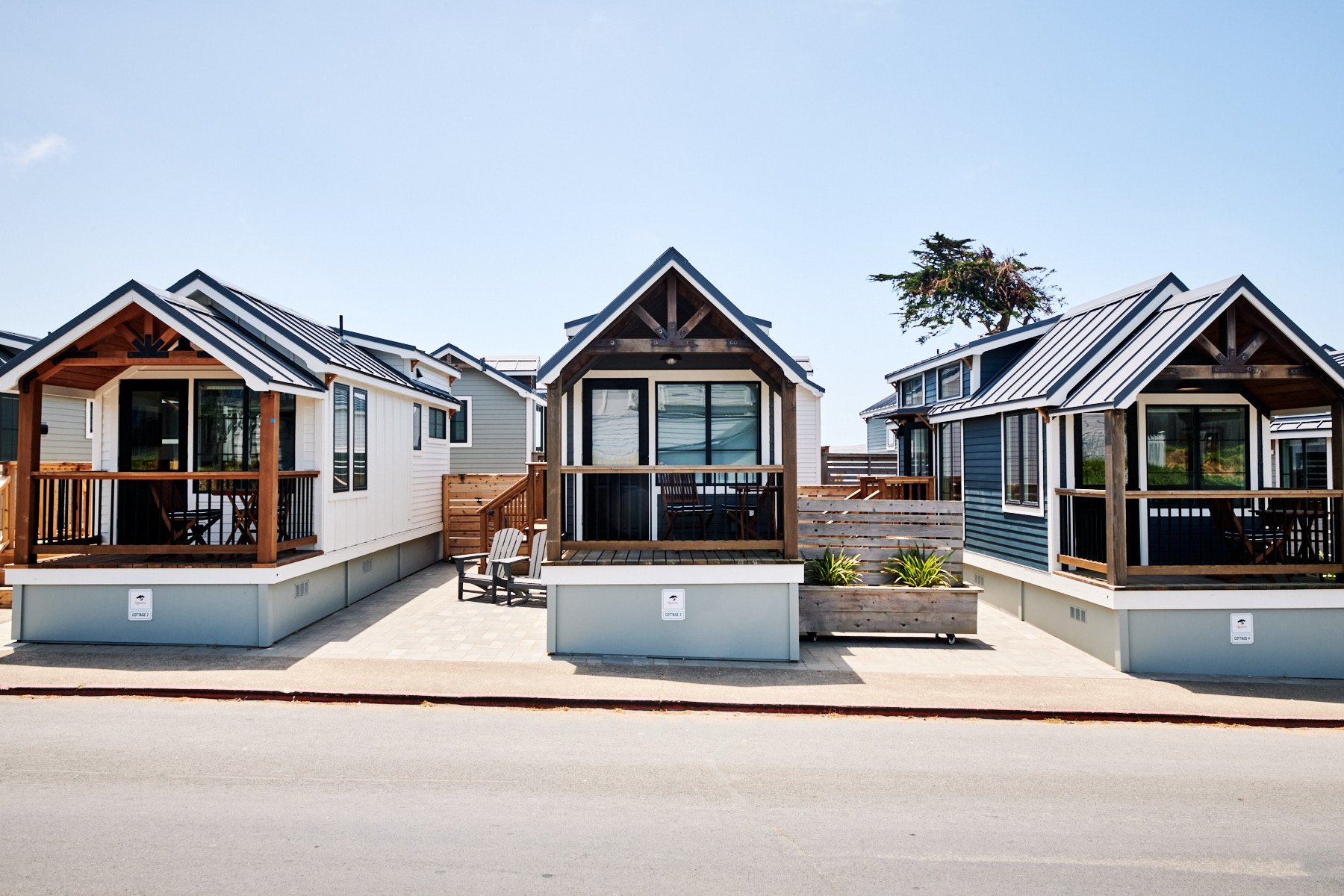 A row of modern Cypress Cottage tiny houses with timber porches and metal roofs under a clear blue sky.