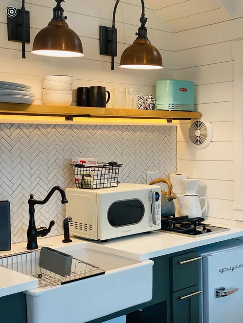 Detail of a compact kitchen featuring a white herringbone tile backsplash, teal retro toaster, and an Insignia microwave on a white countertop.