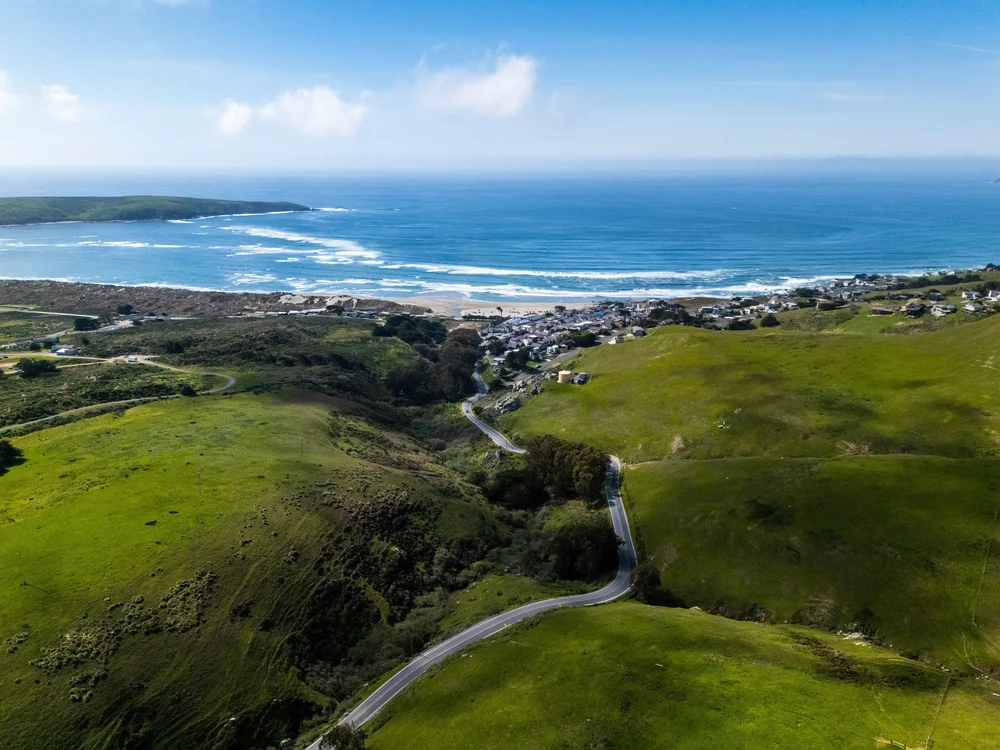 An aerial drone view of ブライトリビエラ’s modern cottages and event grounds, located directly on the coastline with waves crashing on the sandy beach below.